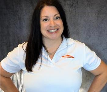 Female employee standing in front of grey backdrop with hands on hips wearing a shirt SERVPRO shirt